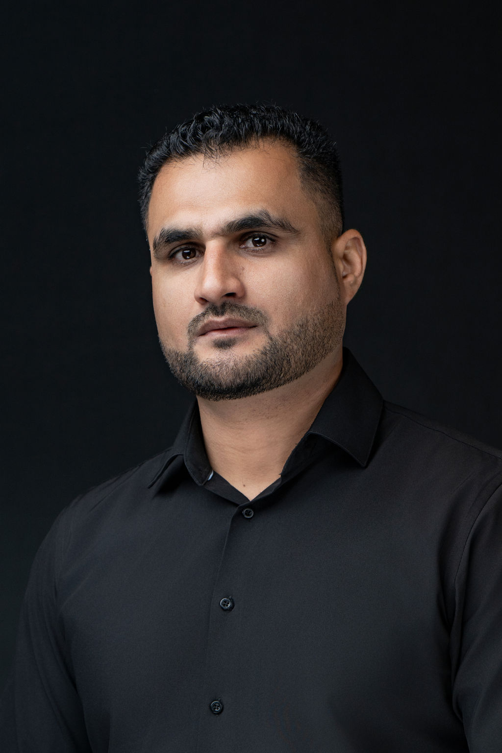 Studio headshot of a man in a black button-down shirt