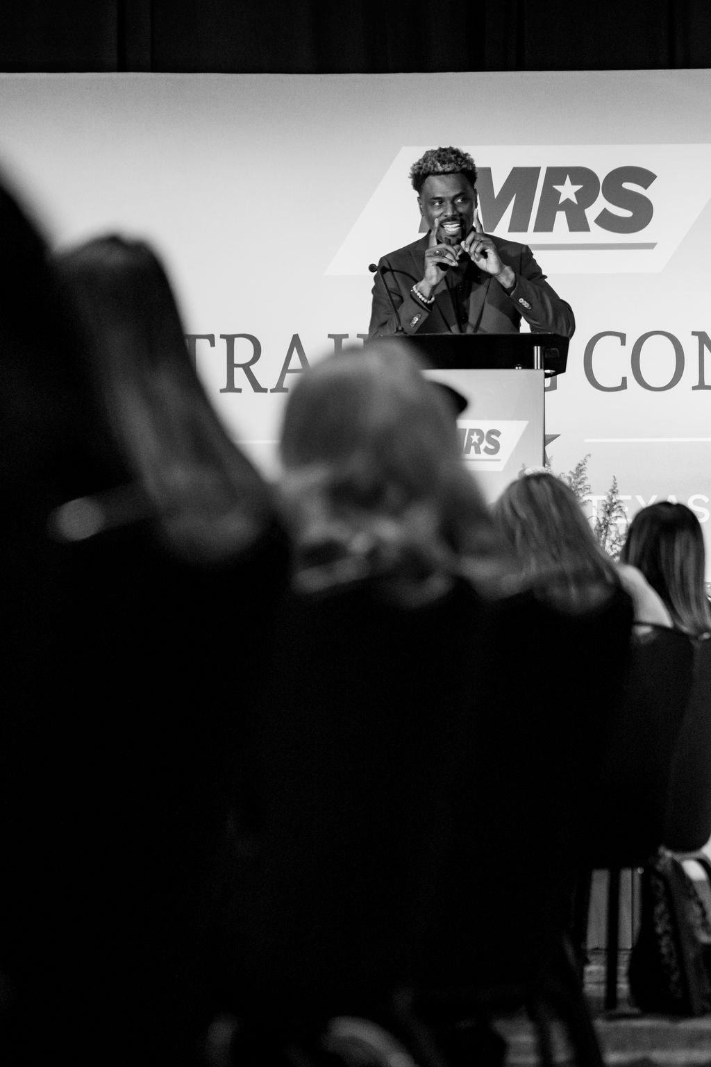 Black and white frame of a keynote speaker at the TMRS podium from the back of the room