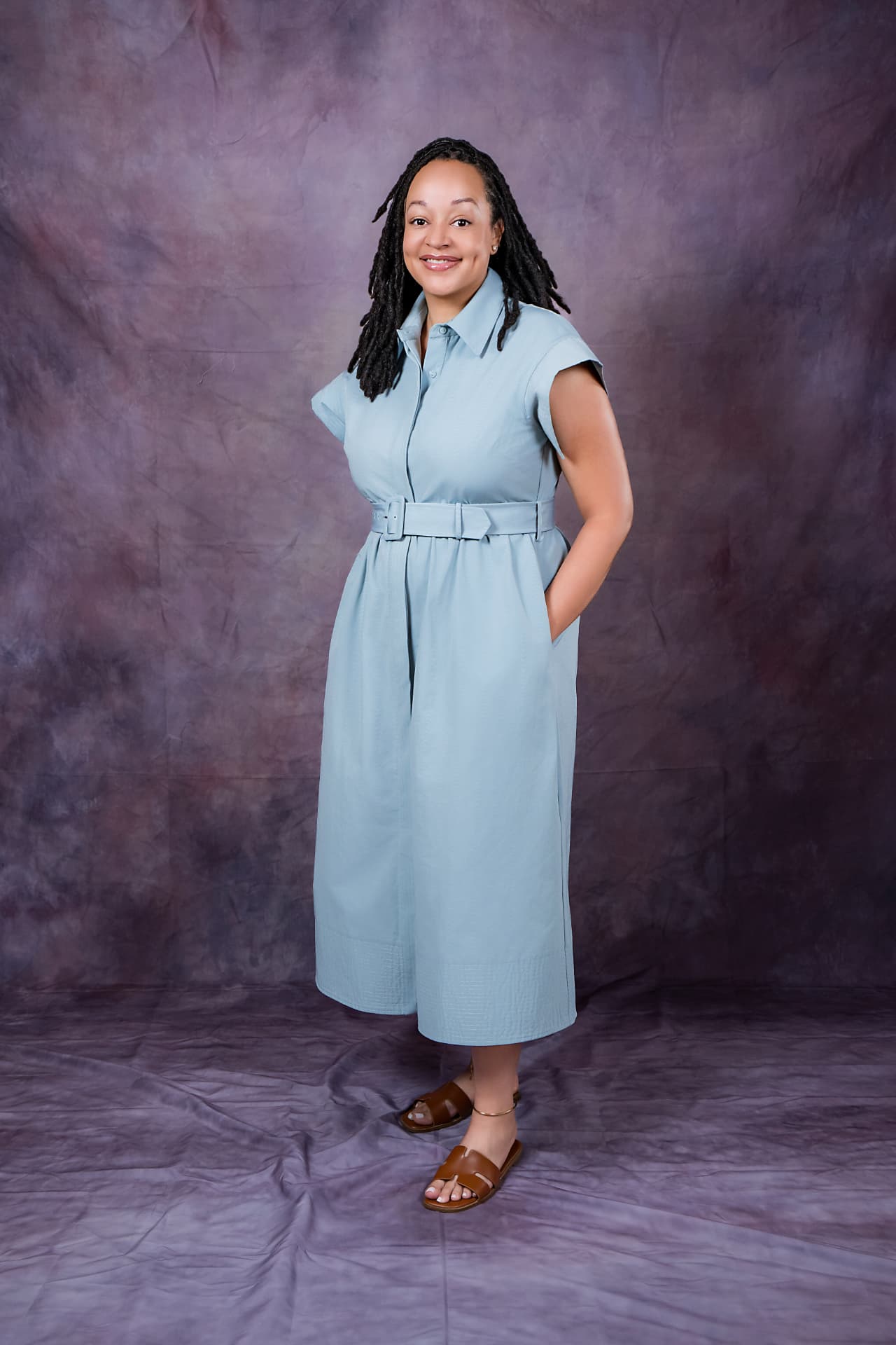 Full-length studio portrait of a smiling woman in a light blue belted dress
