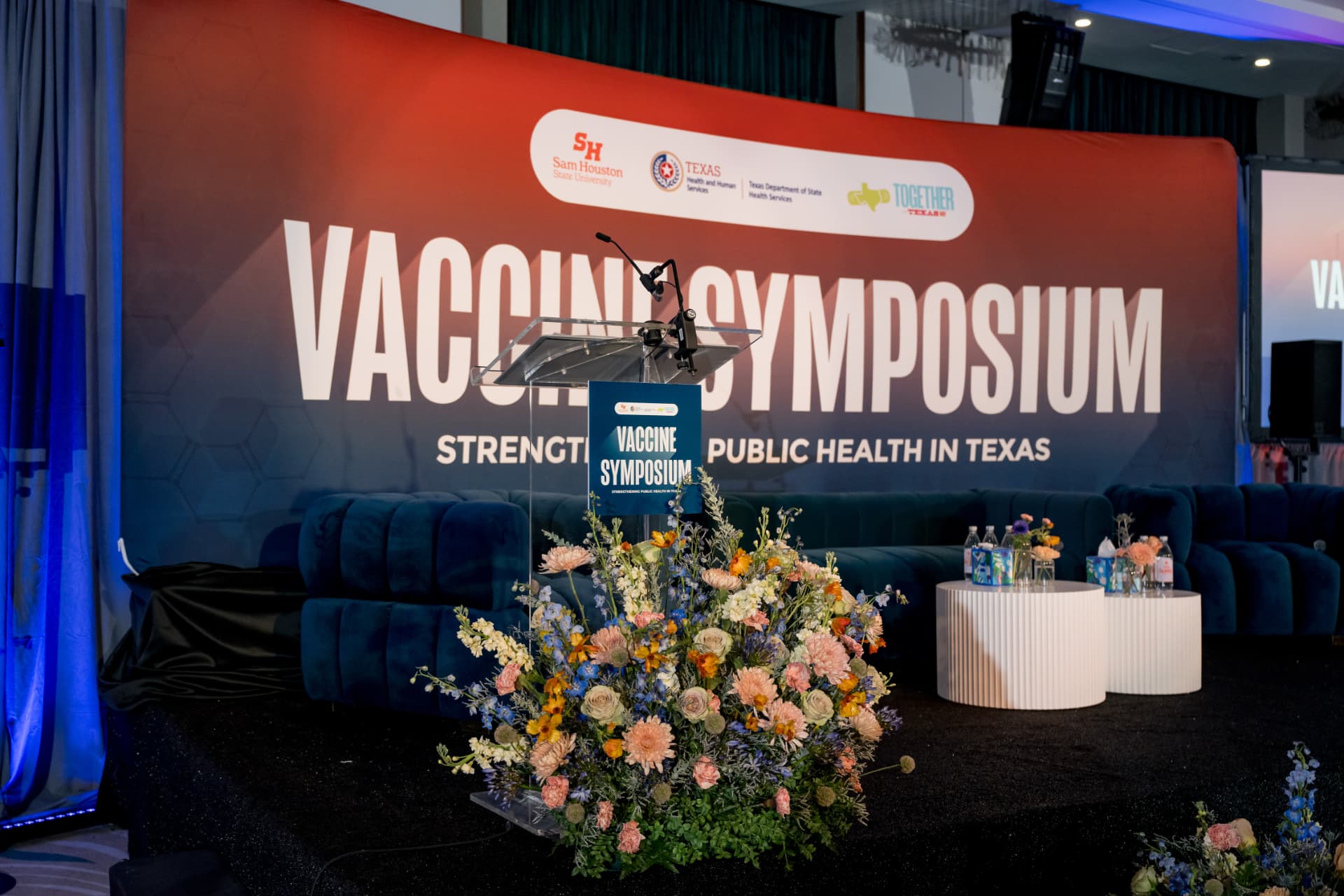 Symposium stage with branded backdrop, podium, and florals