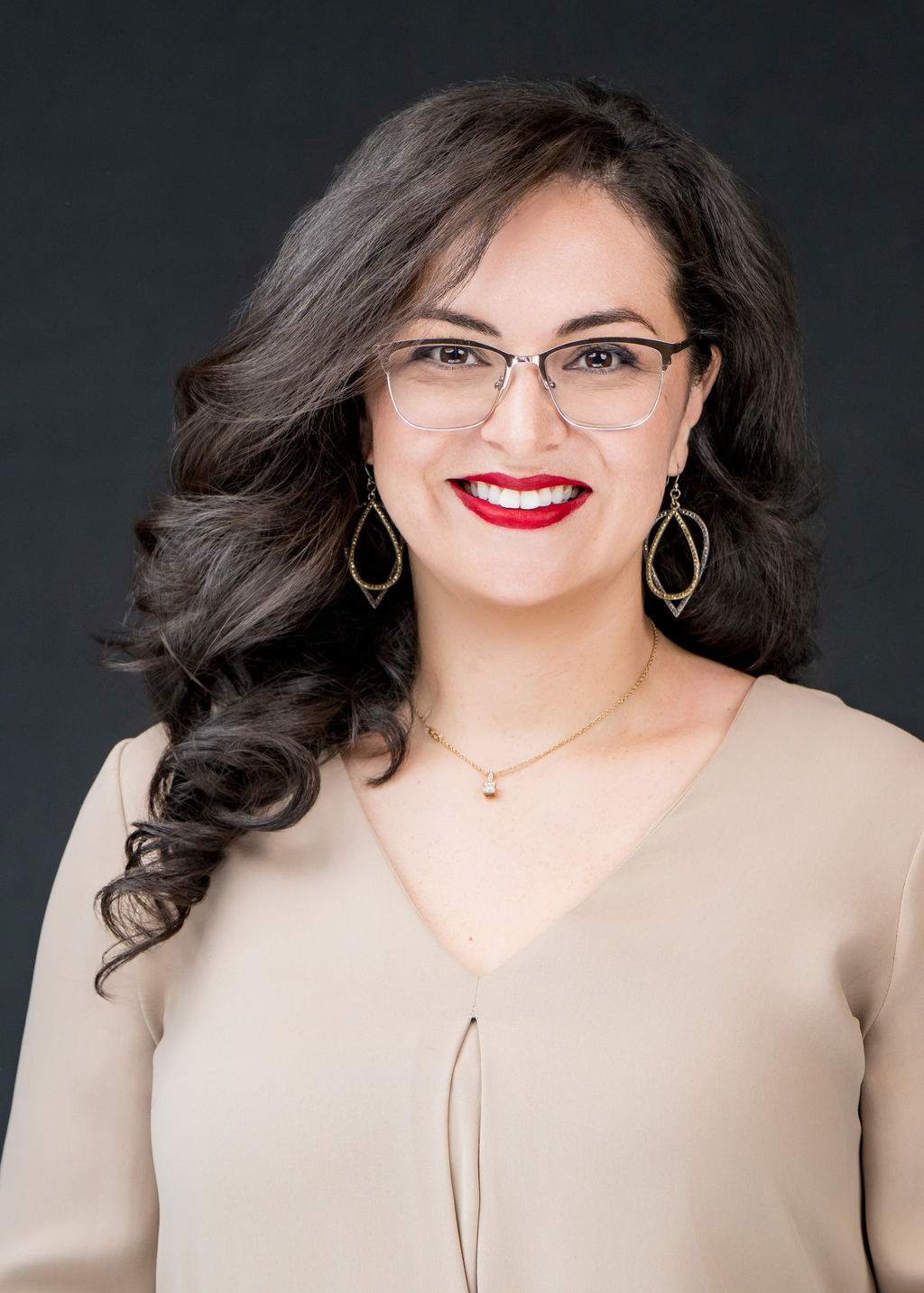 Studio headshot of a woman with wavy dark hair and glasses in a beige blouse