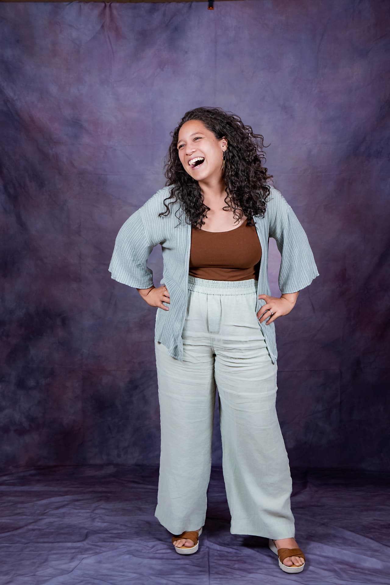 Full-length studio portrait of a laughing woman in a sage linen set
