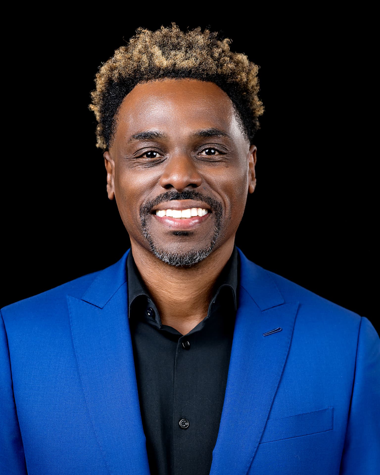 Studio headshot of a smiling man in a bright blue suit jacket