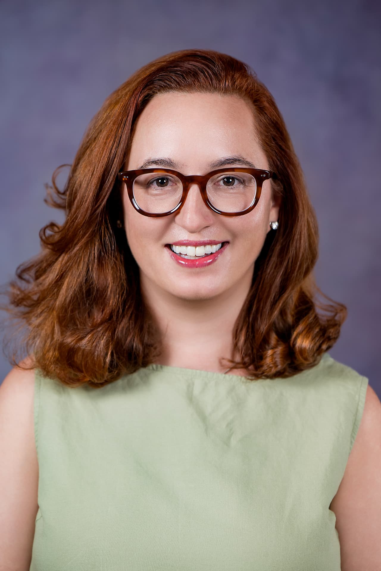 Studio headshot of a smiling woman with auburn hair in a green top