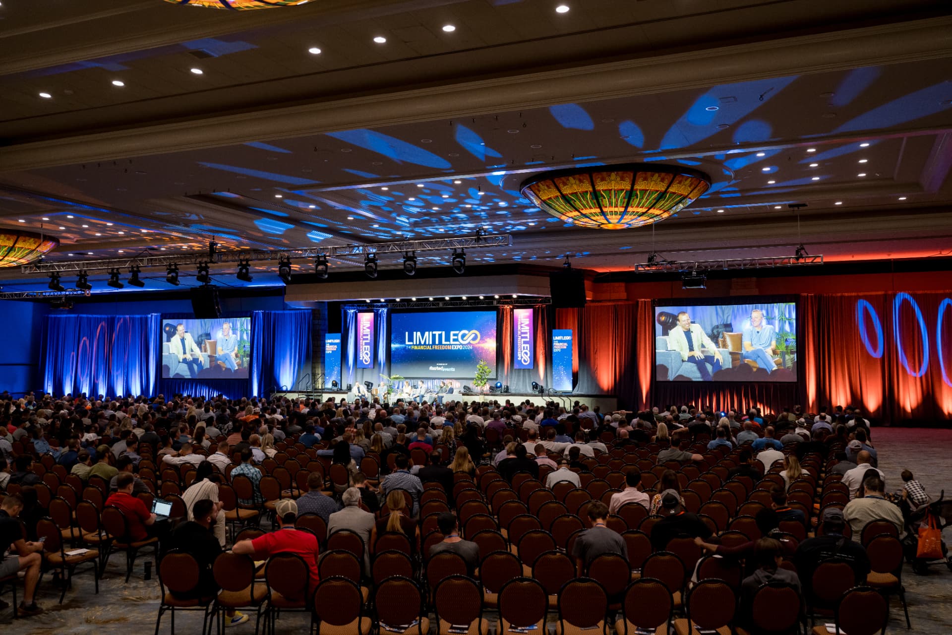Wide ballroom view of the Limitless Expo main stage with dual projection screens