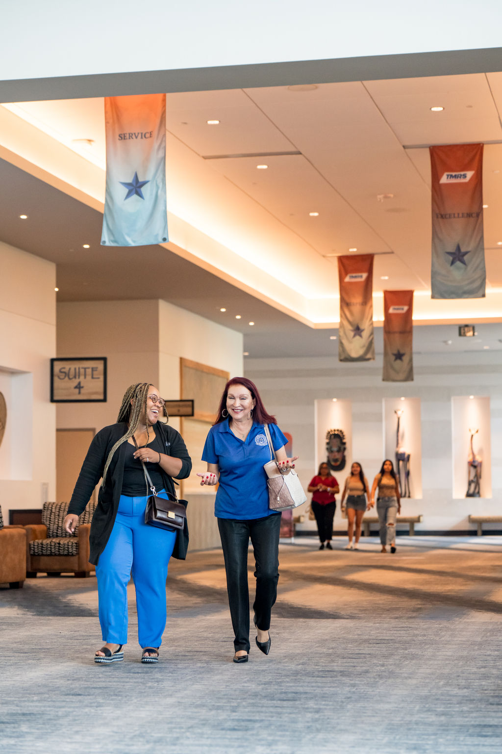 Two attendees walking and laughing beneath TMRS banners in the venue concourse