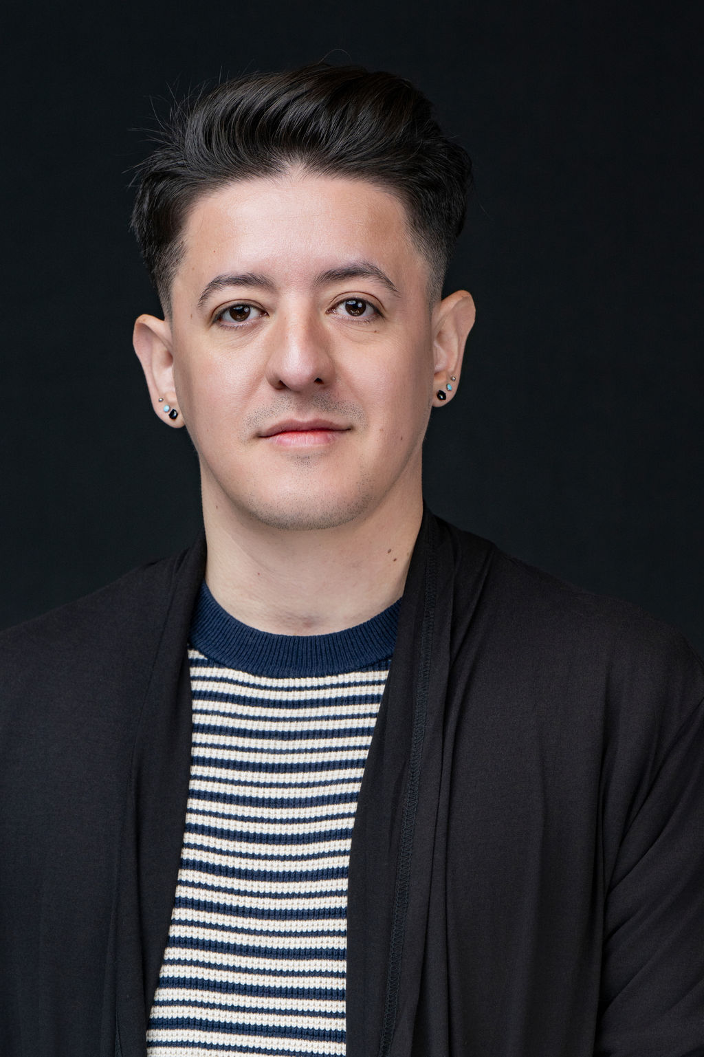 Studio headshot of a man in a black cardigan over a striped sweater