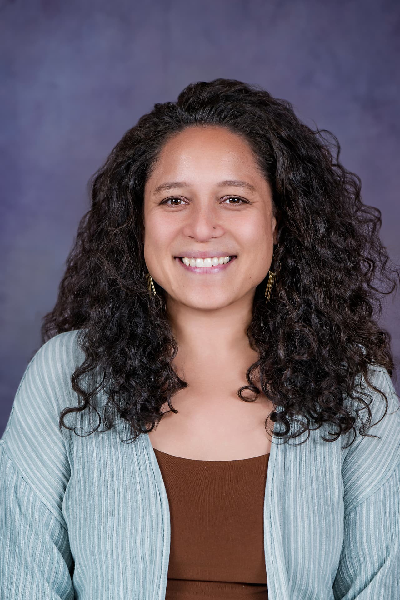 Studio headshot of a smiling woman with curly hair in a sage cardigan