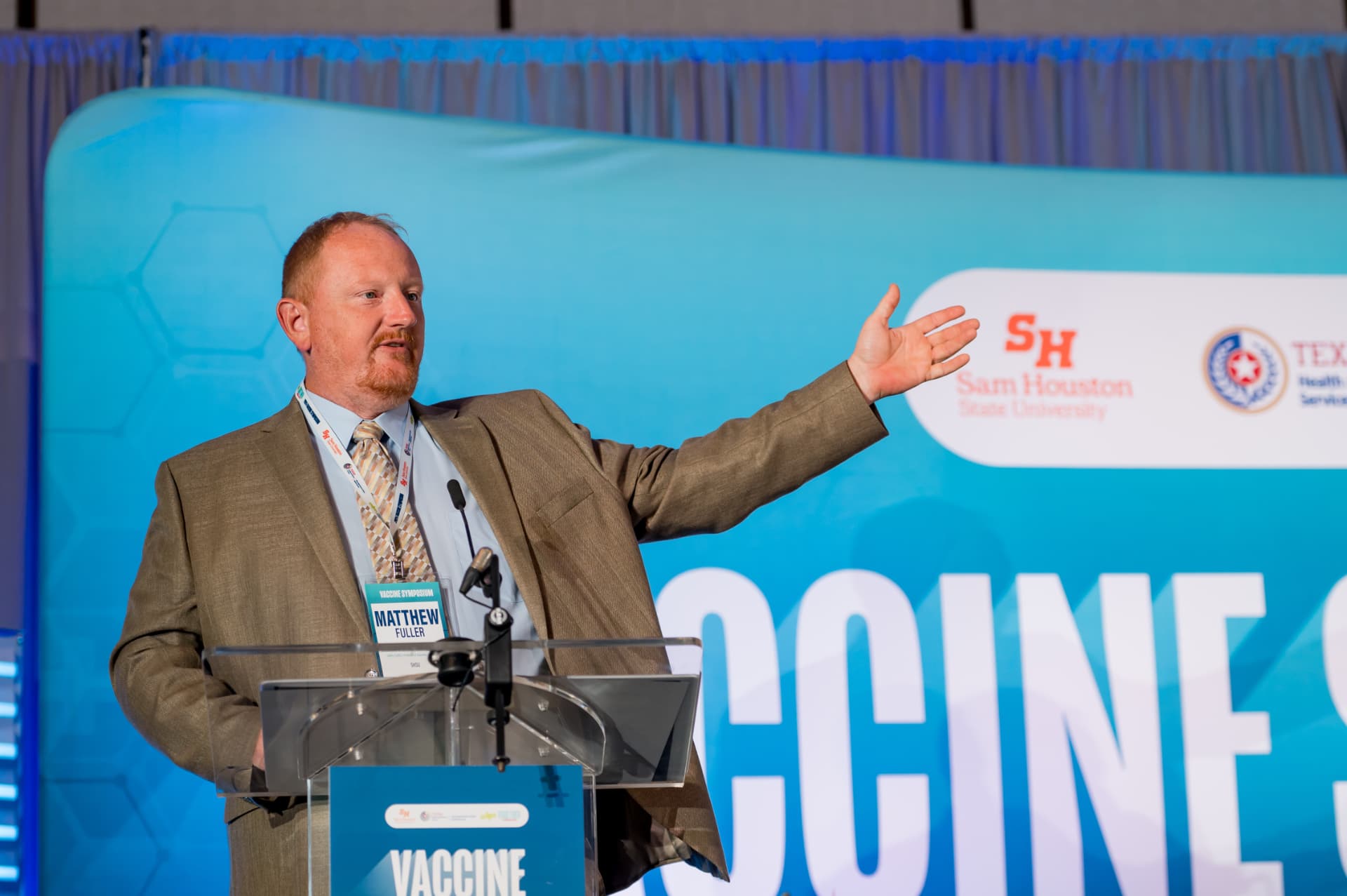 Presenter gesturing on stage at a public health vaccine symposium