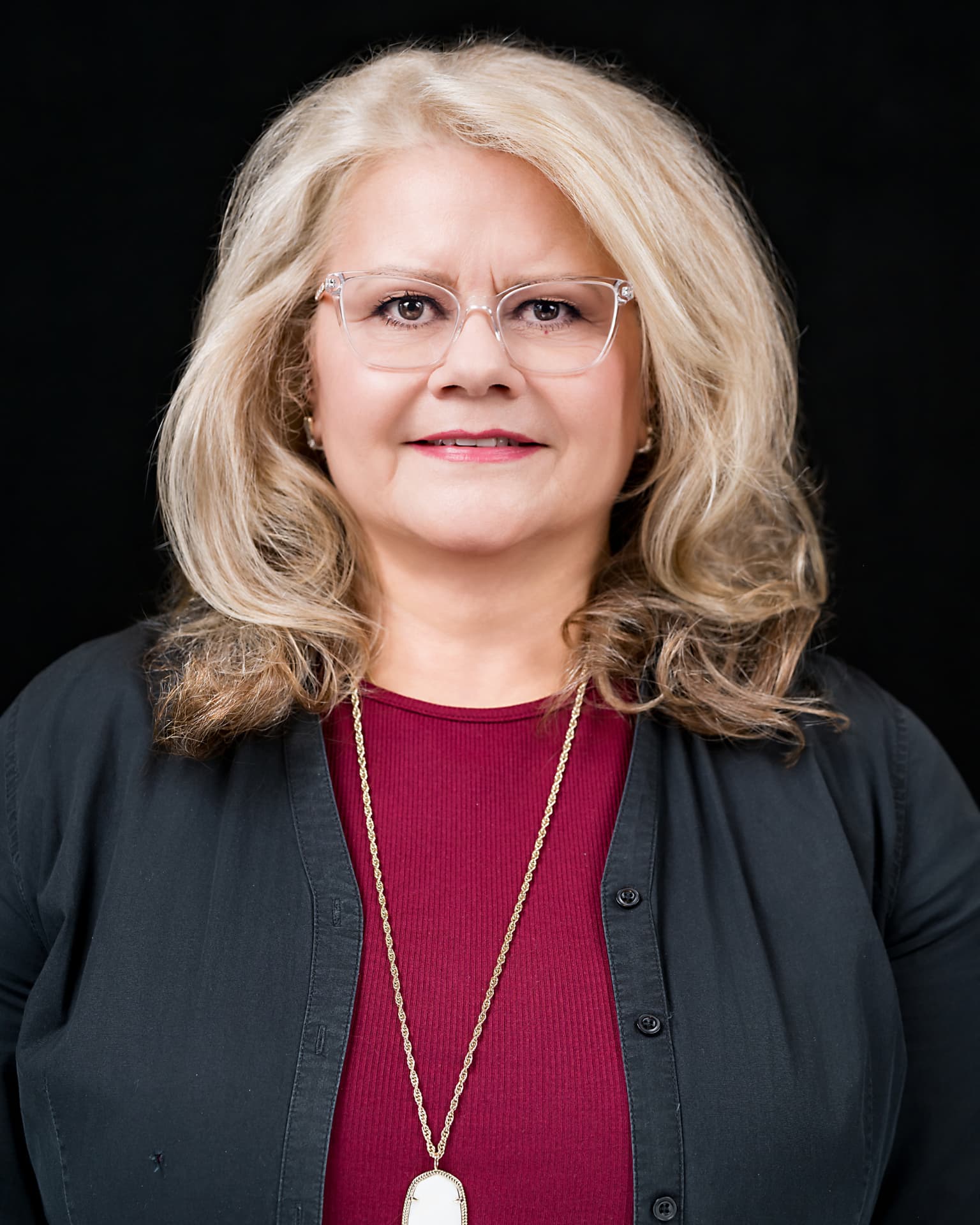 Studio headshot of a professional woman with blonde hair in a dark cardigan