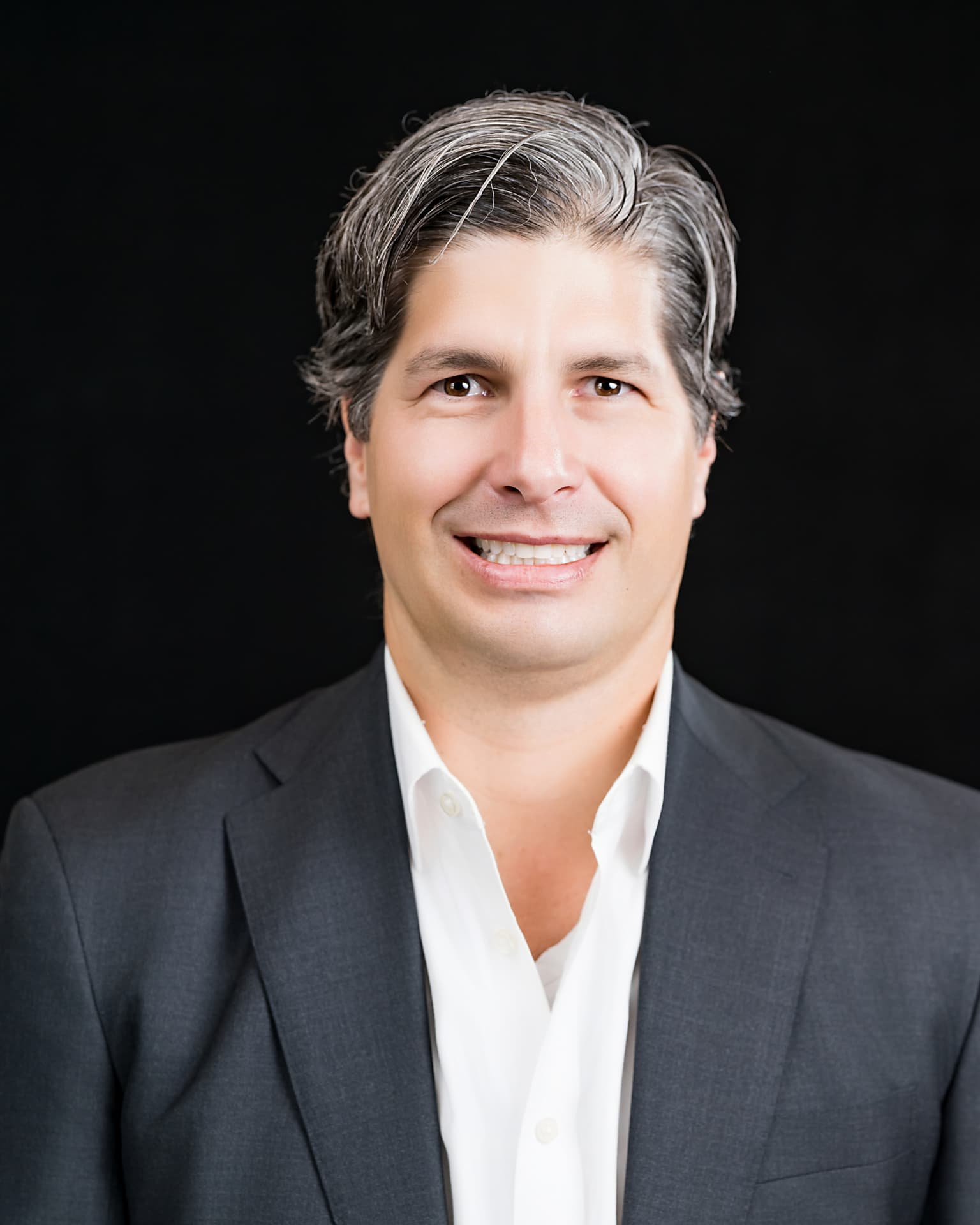 Studio headshot of a professional man in a charcoal suit and open white shirt