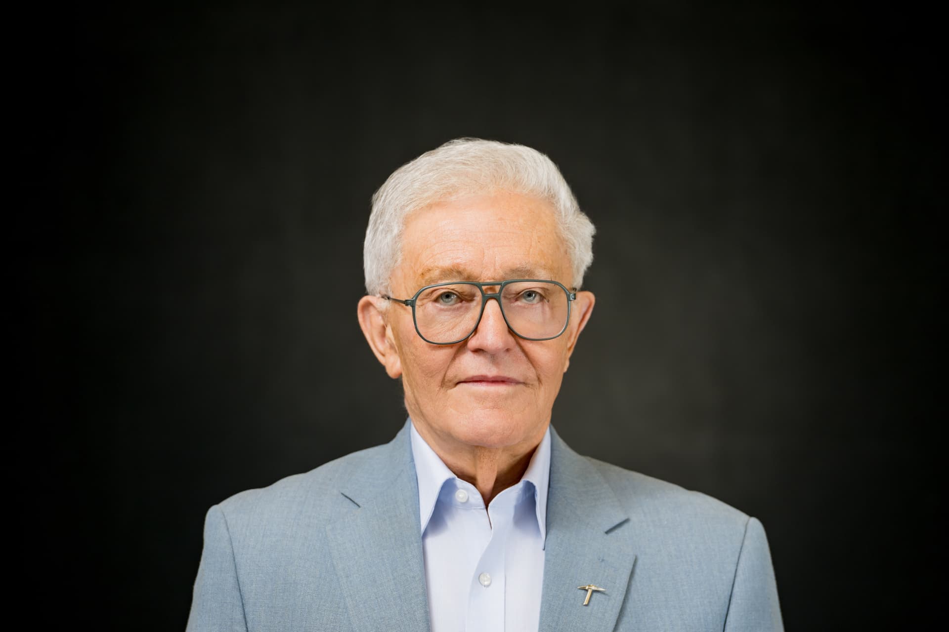 Studio headshot of a senior executive with silver hair in a light grey blazer