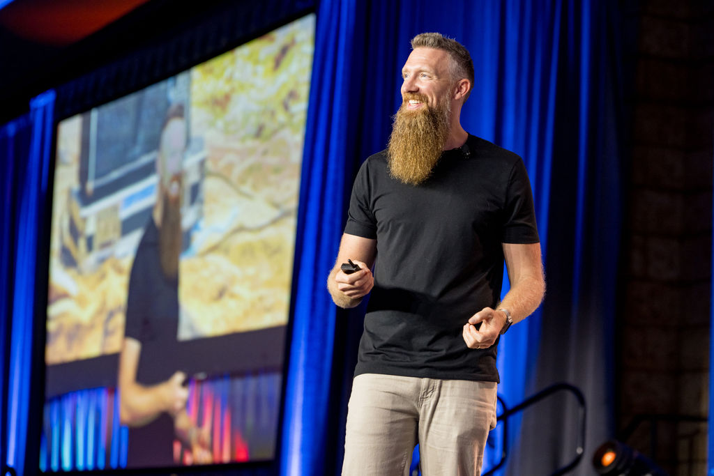 Keynote speaker smiling on stage in front of a large presentation screen at Limitless Expo