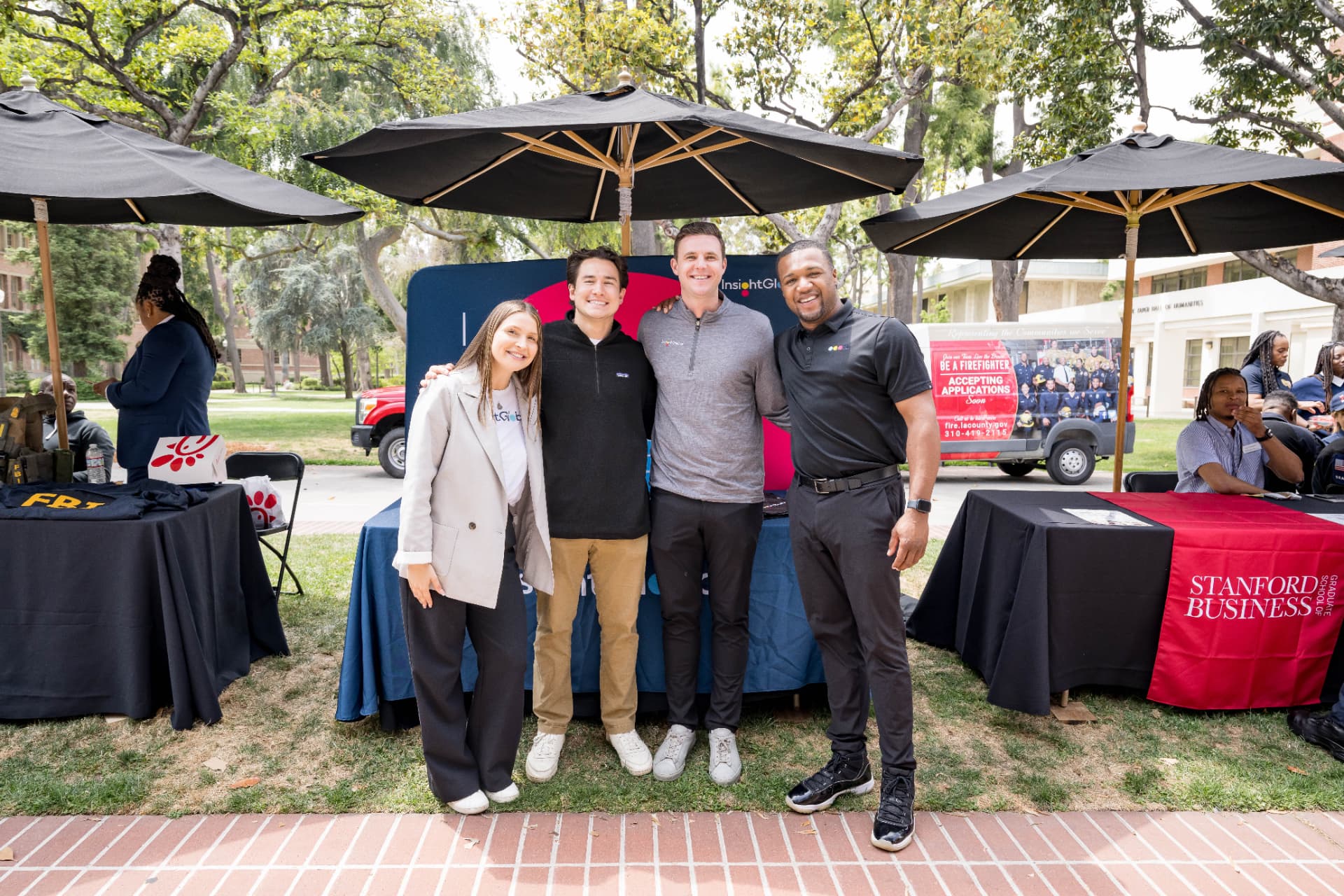 Four exhibitors posing together in front of a sponsor backdrop at a career fair