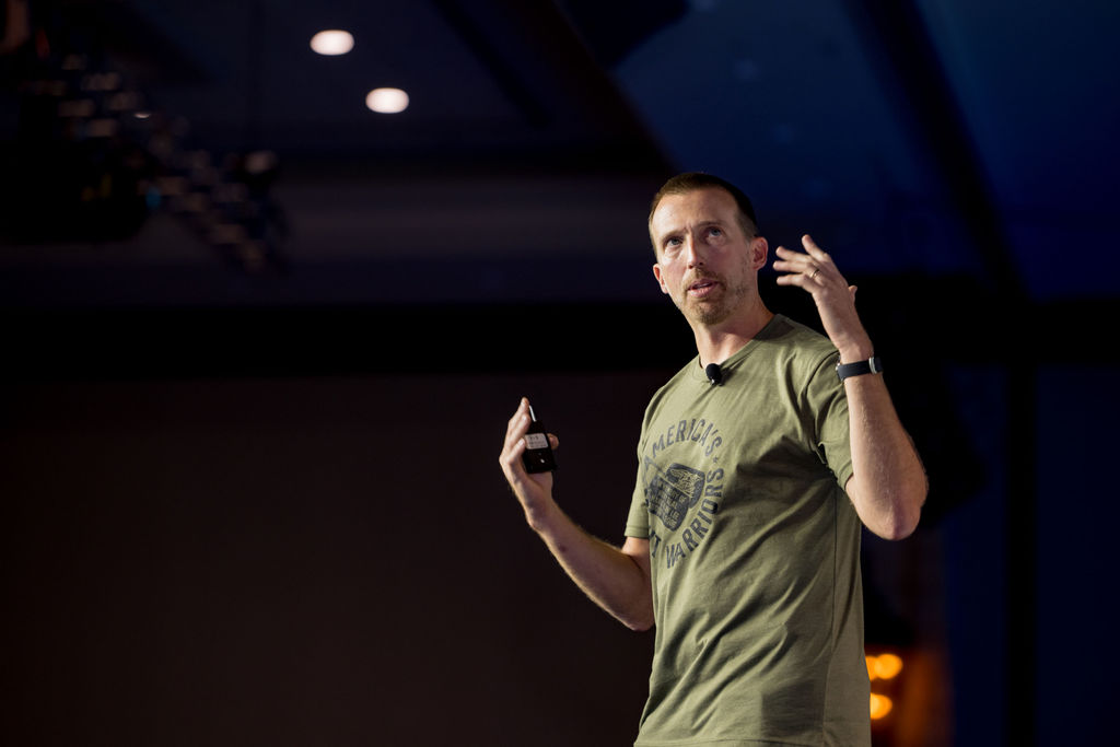 Keynote speaker gesturing under stage lighting at Limitless Expo